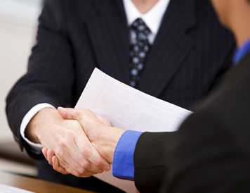 Two smartly dressed business individuals shake hands over a document.
